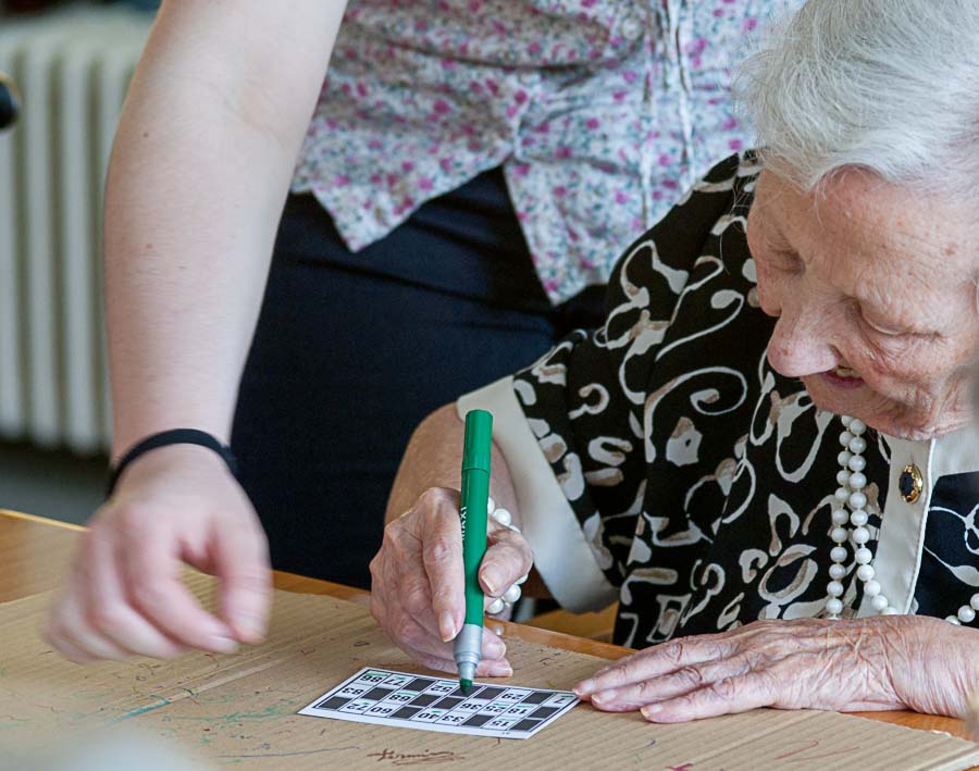 una residente rellena una tarjeta de bingo con la ayuda de una auxiliar